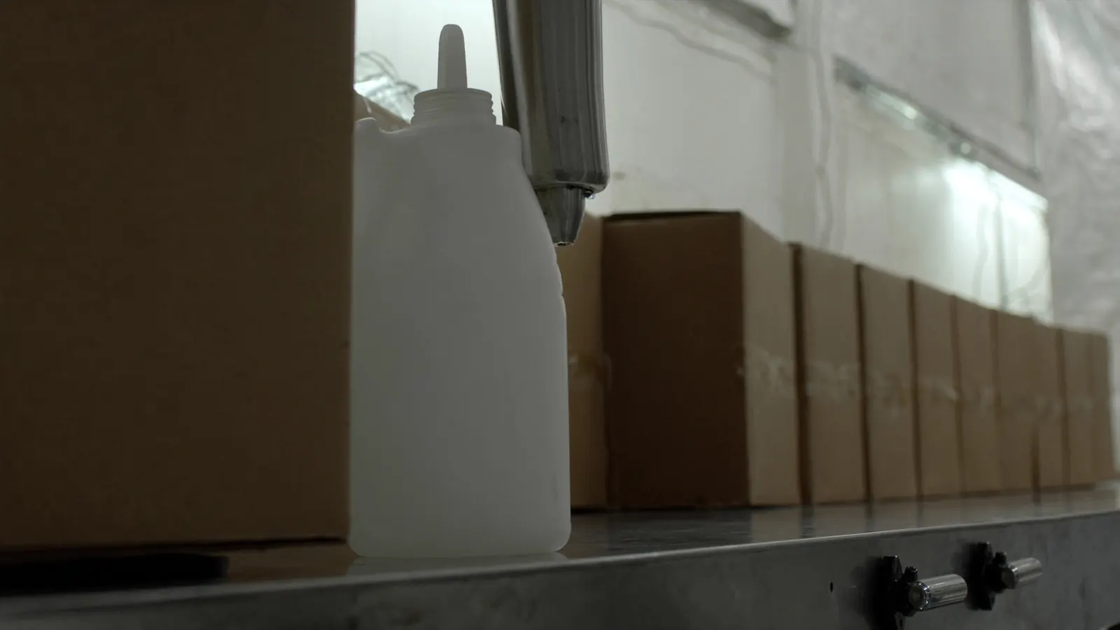 A jug under a filling head with cases behind it